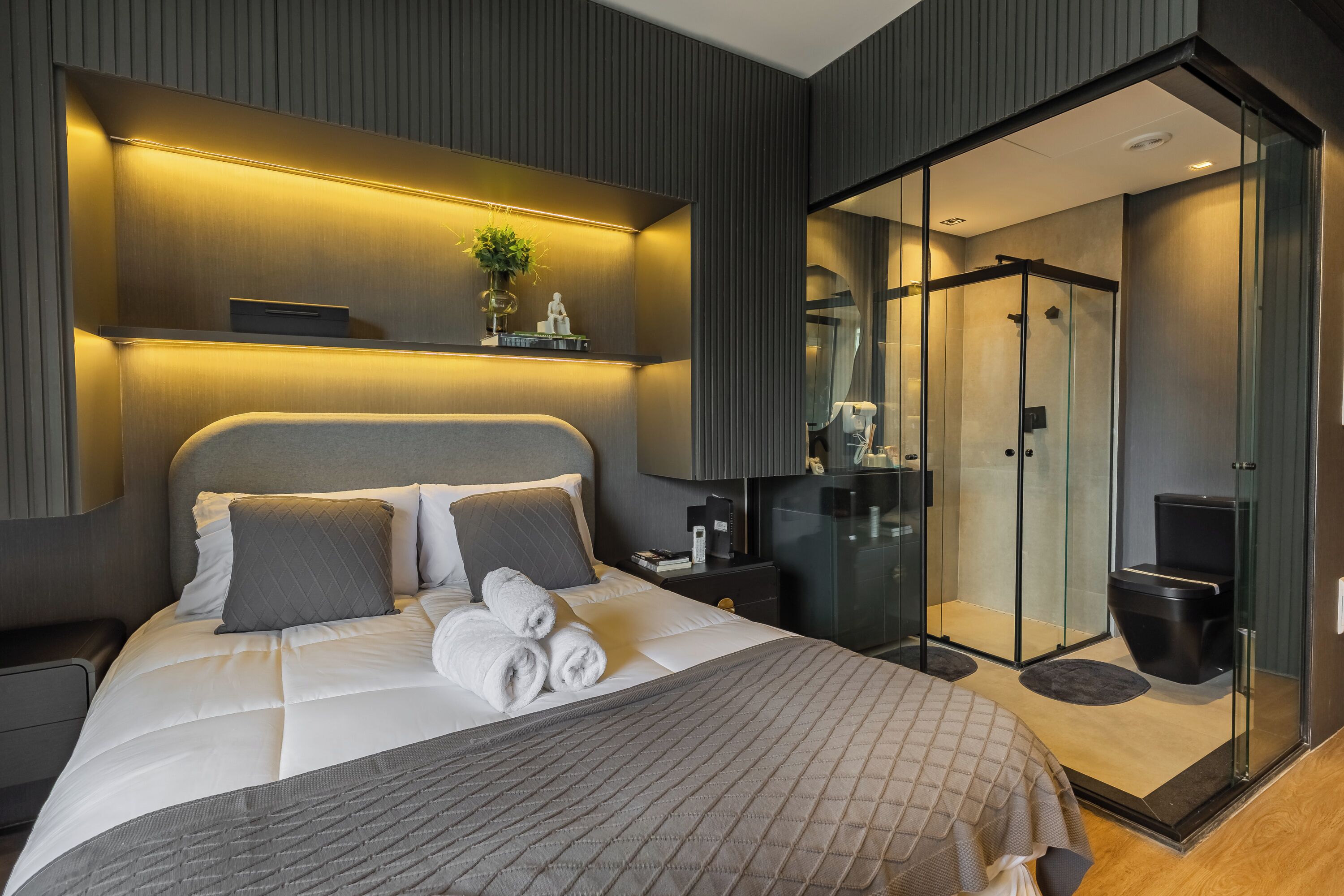 Ein modernes Hotelzimmer mit einem großen Bett, Nachttischen, einer Duschkabine aus Glas und einer kleinen Sitzecke.