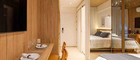 Una habitación de hotel moderna con una zona de comedor de madera, una cama con cabecero y un espejo grande.