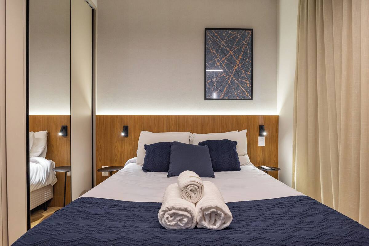 A hotel room with a bed, two bedside tables, a wall-mounted artwork, and a curtain.