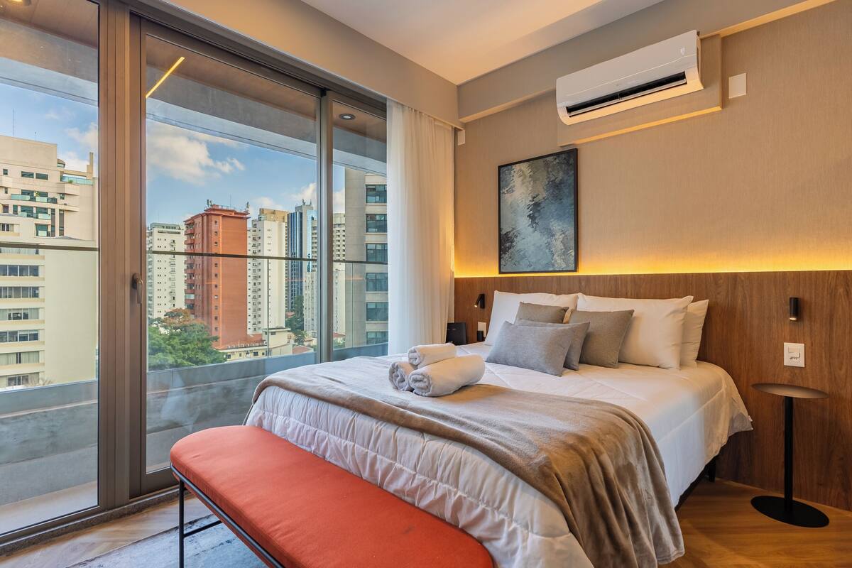 Une chambre d’hôtel moderne dotée d’une grande fenêtre, d’un lit avec des oreillers, d’une table de chevet et d’un appareil de climatisation.