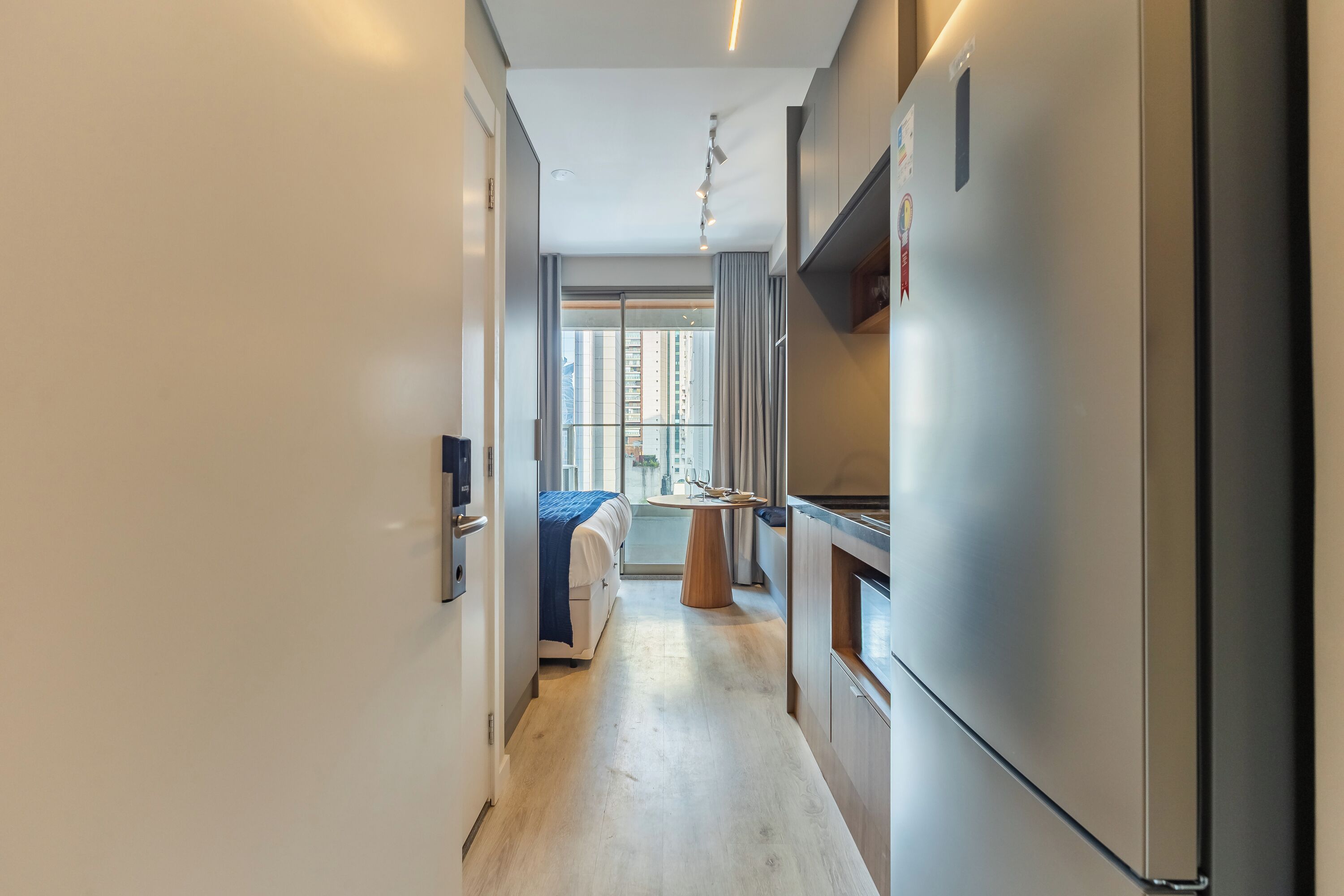 A narrow hallway with a bed, a small table, and a refrigerator.