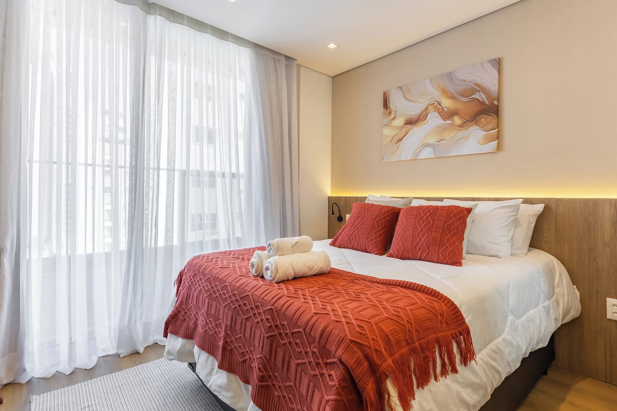 A neatly made bed with a red blanket, white pillows, and a headboard with a light fixture.