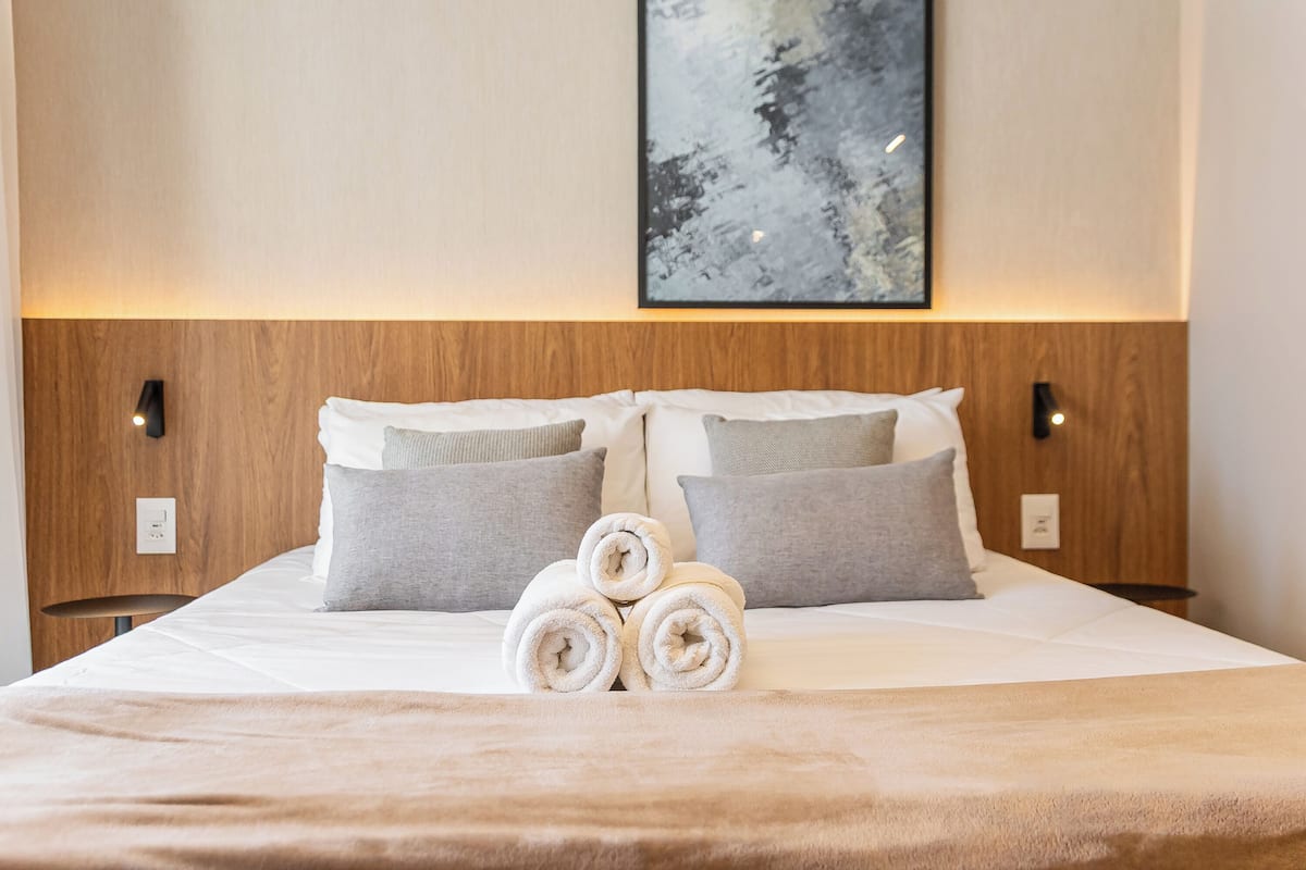 A neatly made bed with rolled towels, two pillows, and a wall-mounted abstract painting.