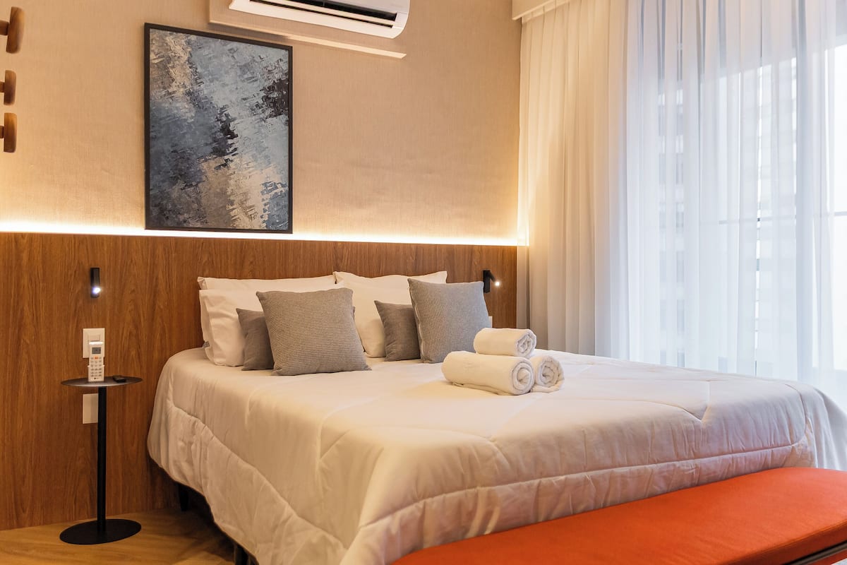 Une chambre d’hôtel avec un lit, une table de chevet avec un téléphone, un tableau au mur et une fenêtre avec des rideaux.