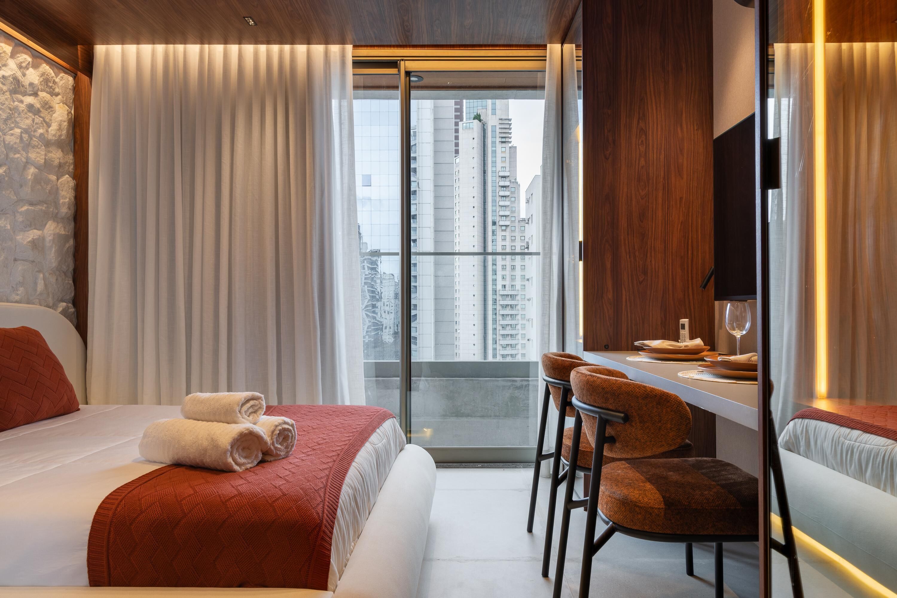 Une chambre d’hôtel avec un lit, un bureau avec des chaises, une télévision et une vue sur de hauts immeubles.