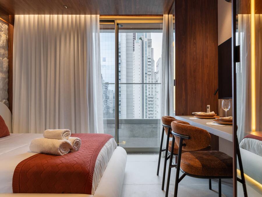 Une chambre d’hôtel avec un lit, un bureau avec des chaises, une télévision et une vue sur de hauts immeubles.