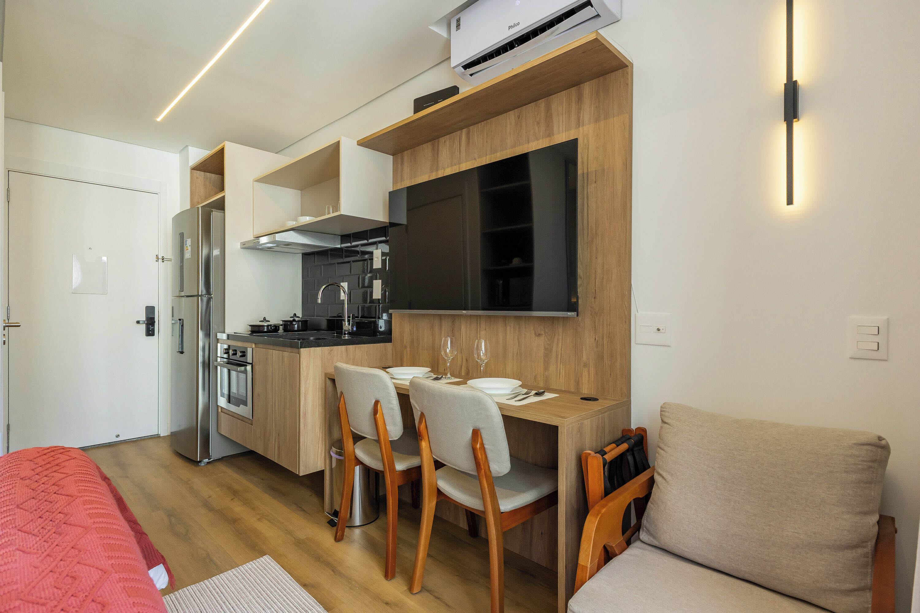 A compact kitchen with a refrigerator, stove, and microwave. There is a dining area with chairs and a table.