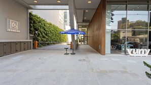 A modern building entrance with a blue umbrella, a sign for 'JEROMINO', and a 'VUNY' sign. - Stay Home Luxo Itaim (São Paulo)