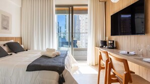 Une chambre d’hôtel avec un lit, un bureau doté d’une machine à café, une télévision et une vue sur la ville grâce à de grandes fenêtres.