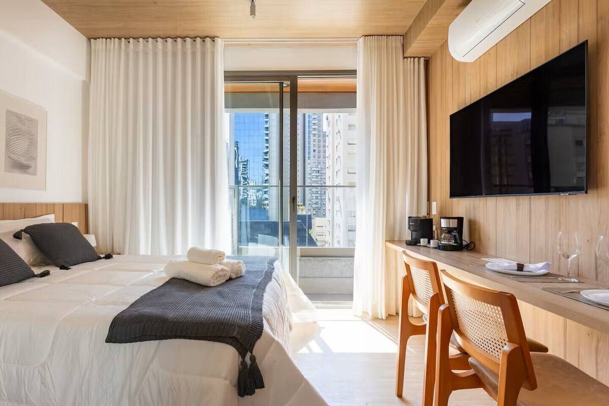 Une chambre d’hôtel avec un lit, un bureau doté d’une machine à café, une télévision et une vue sur la ville grâce à de grandes fenêtres.