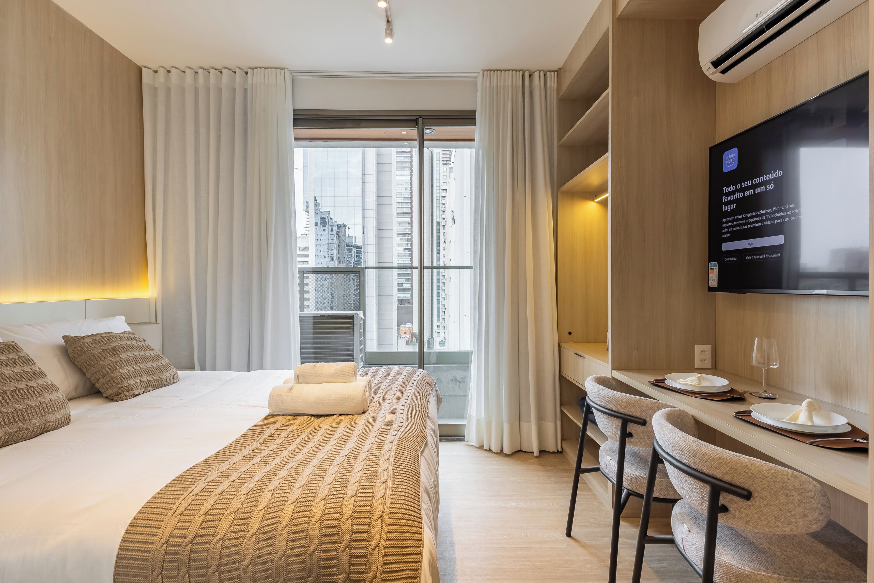 Une chambre d’hôtel comprenant un lit, un bureau avec des chaises, une télévision et une grande fenêtre avec des rideaux.