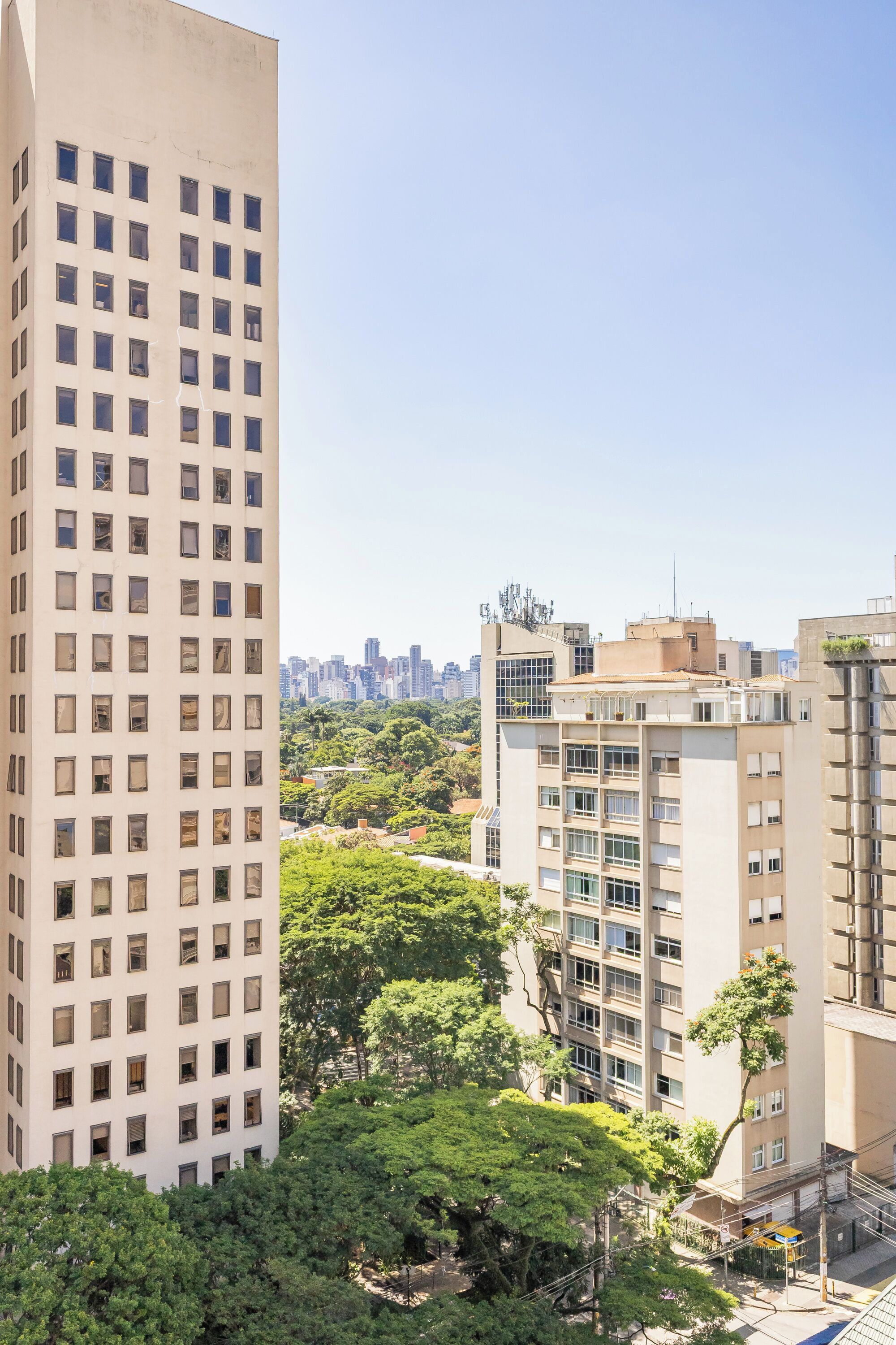 A high-rise building with multiple windows, surrounded by greenery and other buildings.