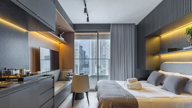 Une chambre d’hôtel moderne, dotée d’un grand lit, d’un bureau, d’une chaise et offrant une vue sur le paysage urbain.