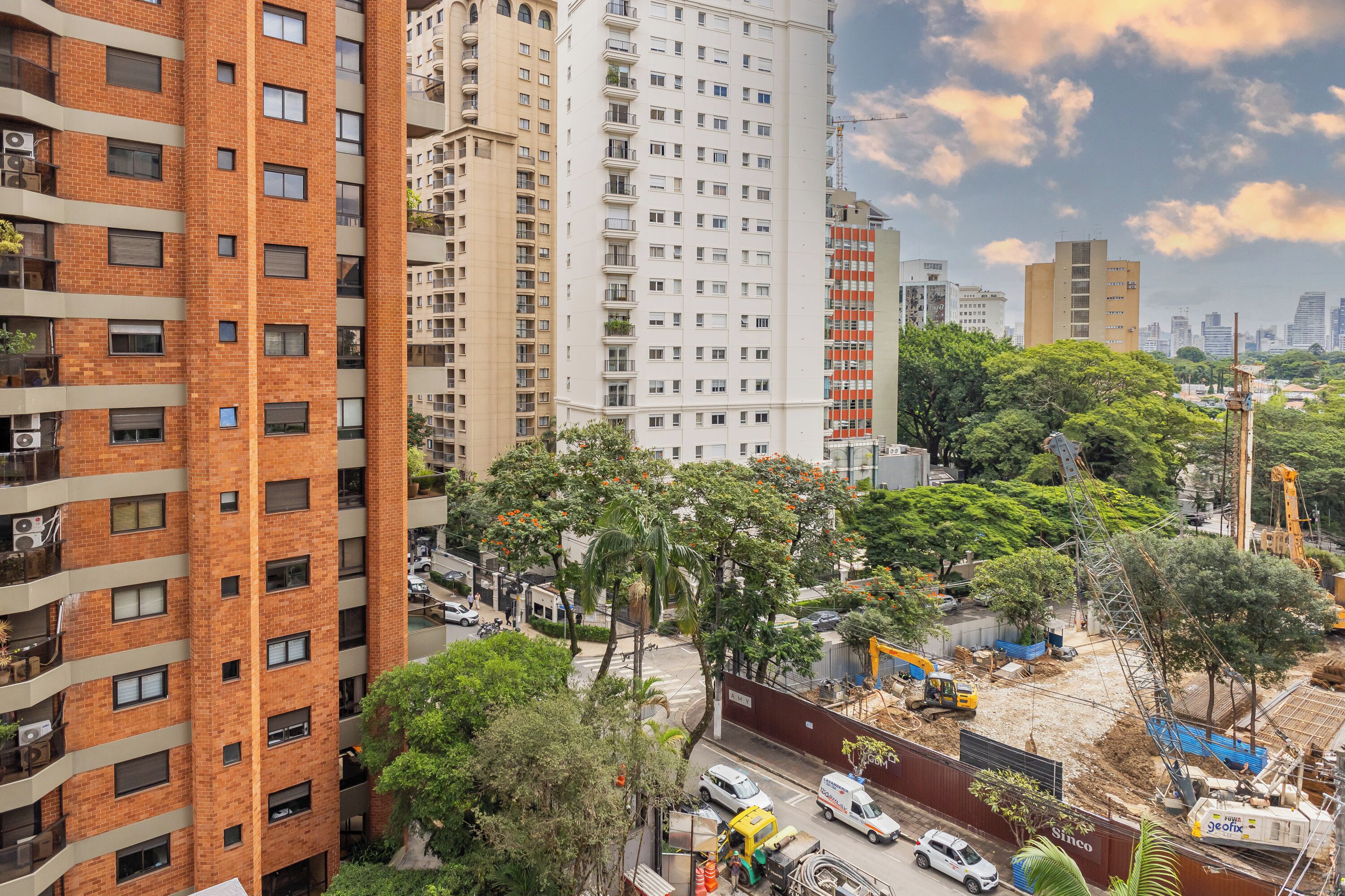 A multi-story building with a brick facade, surrounded by greenery and construction equipment.