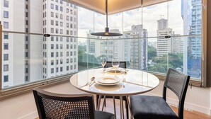 Un espace de salle à manger moderne avec une table ronde, des chaises noires et une vue sur la ville grâce à de grandes fenêtres.