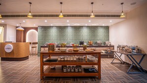 A reception area with a reception desk, seating, a buffet table with food and drinks, and a tiled backsplash. - Mosaic Connect Ayodhya (Faizabad)