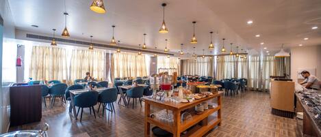 Un grand espace dédié à la salle à manger, avec plusieurs tables et chaises, un éclairage au plafond et un buffet.