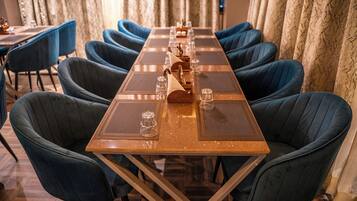 A long dining table with blue upholstered chairs, a wooden table runner, and clear glassware.