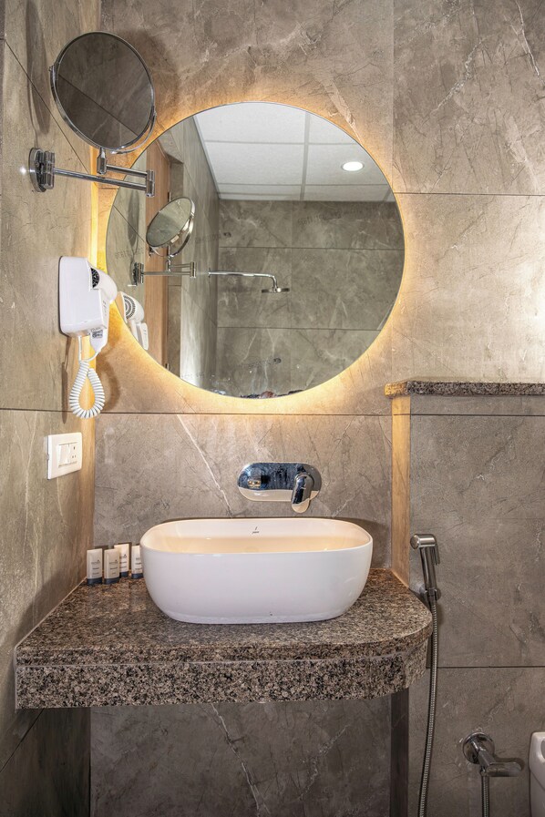 Un baño con espejo redondo, lavabo, secador de pelo y ducha.