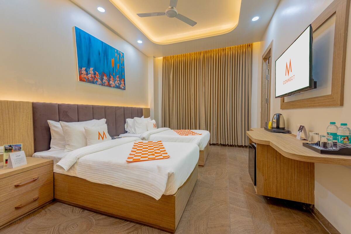 A hotel room with two beds, a desk, a TV, and a ceiling fan.