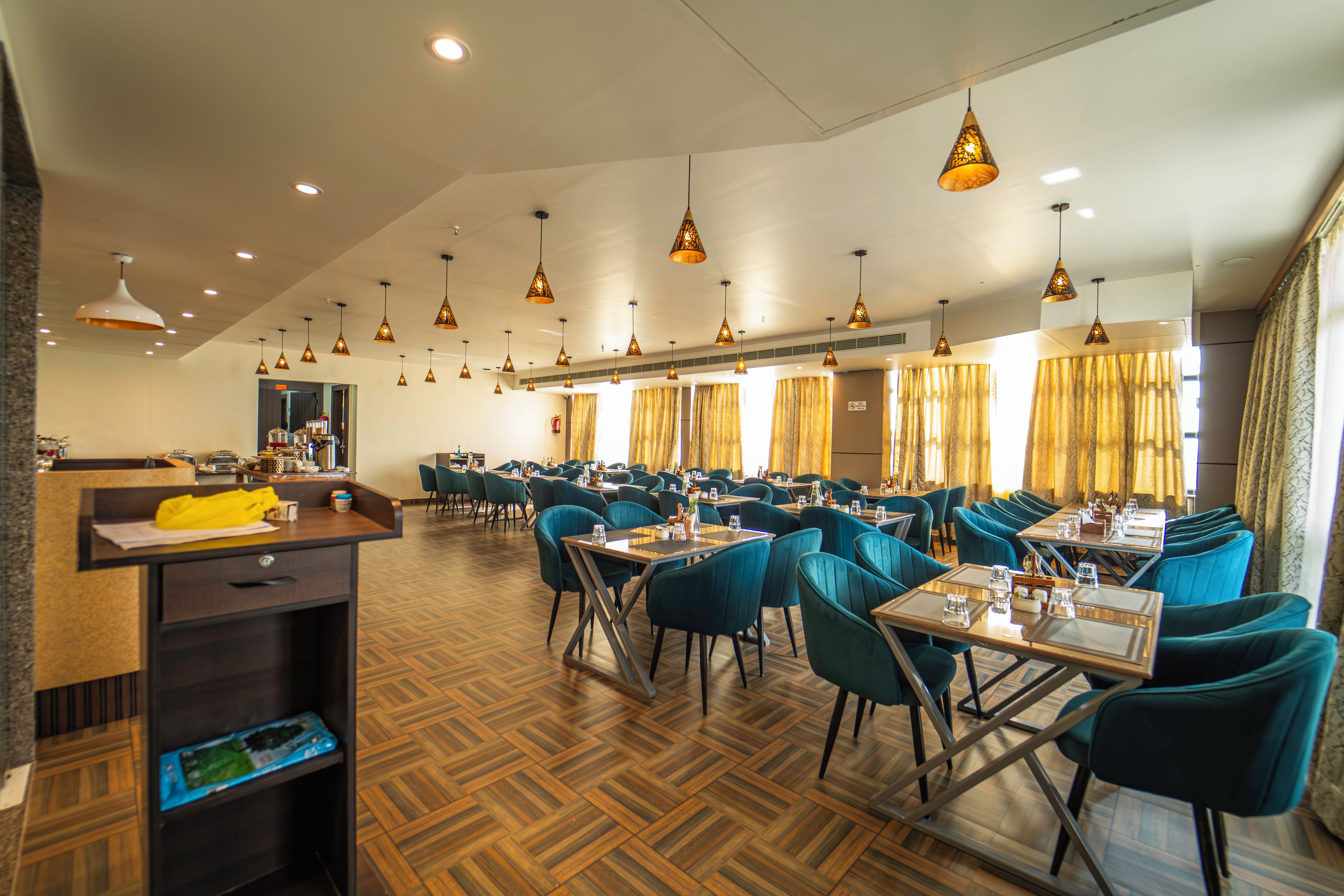 A spacious dining area with multiple tables and chairs, overhead lighting, and a herringbone patterned floor.