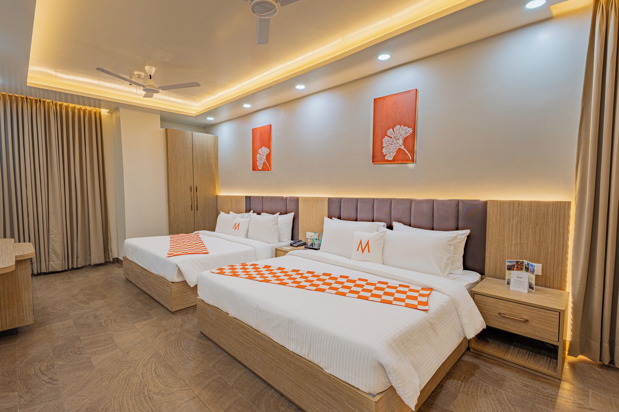 A hotel room with two beds, a desk, a wardrobe, and a ceiling fan.