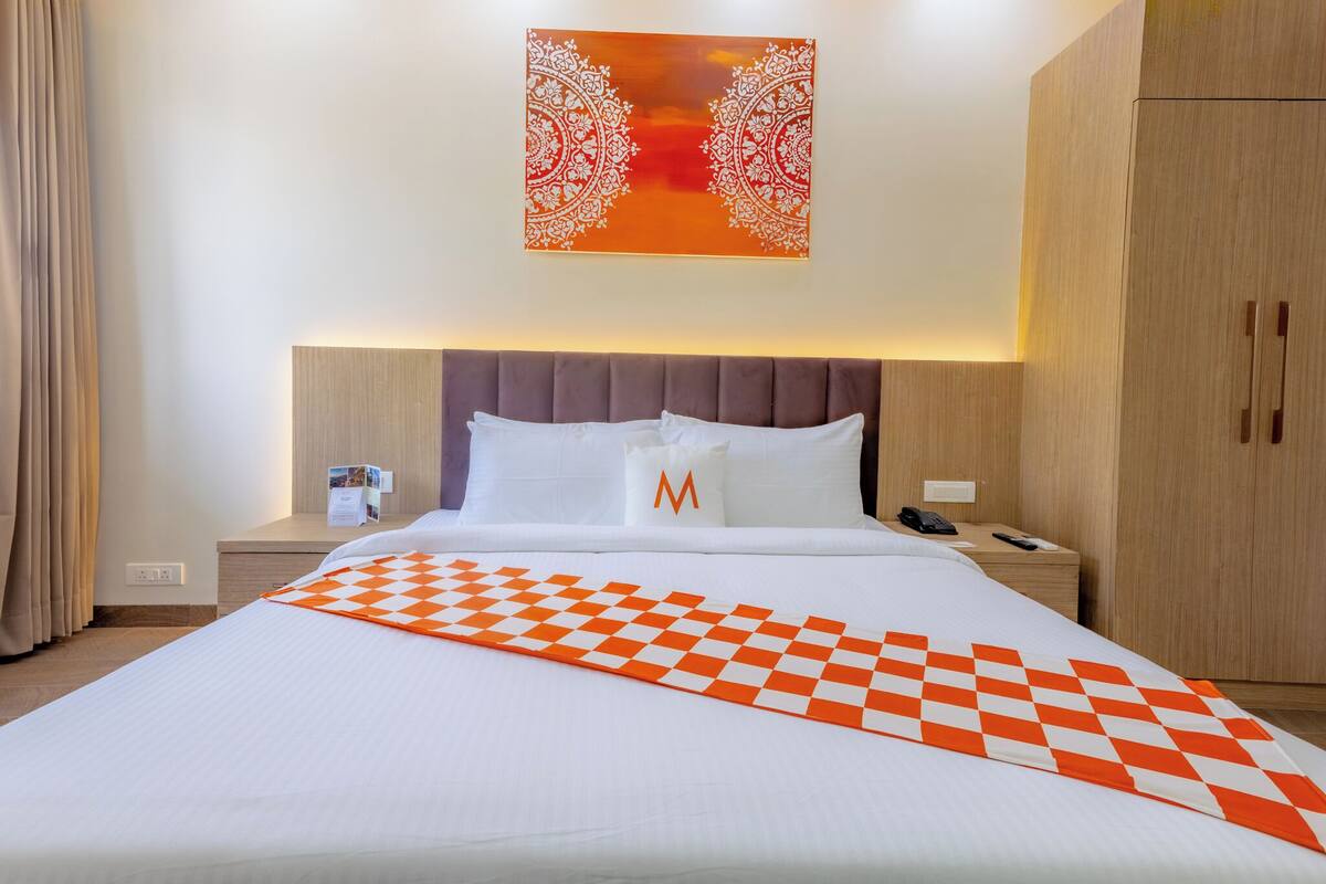 A hotel room with a large bed, a nightstand with a phone, a wall-mounted artwork, and a wardrobe.