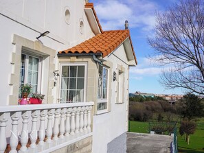 Un bâtiment blanc avec un toit recouvert de tuiles, un balcon orné de balustres et une vue sur un paysage verdoyant.