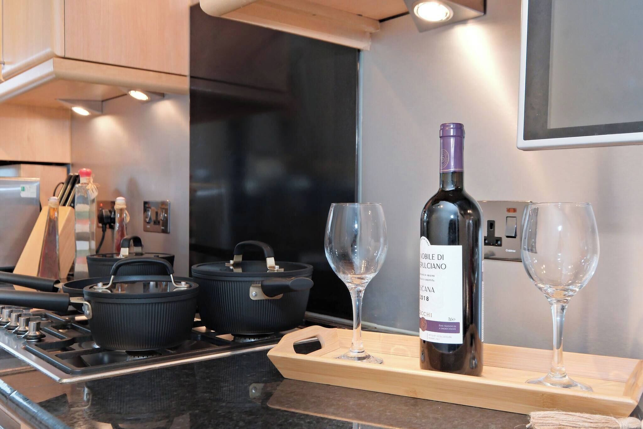 Una cocina con estufa, ollas, una botella de vino y copas sobre una bandeja.