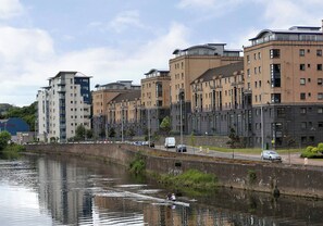 Une rivière, de l’autre côté de laquelle se trouvent des bâtiments, notamment une haute structure dotée de balcons et un bâtiment plus petit avec un toit plat.