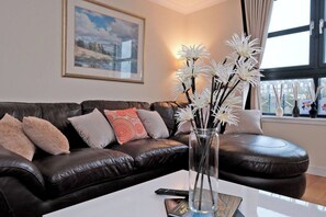 A living room with a dark brown leather sofa, a vase with white flowers, and a framed picture on the wall. - Executive 2bed City Centre Apartment in Aberdeen (Aberdeen)