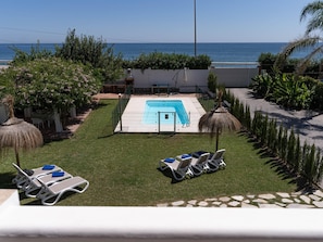 A swimming pool with a view of the sea, surrounded by grass and palm trees. - Beachfront apartment with communal pool and parking in San Pedro de Alcántara (San Pedro Alcántara)