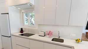 Ett modernt kök med vita skåp, en inbyggd ugn, en diskho och ett fönster med utsikt över grönområden.