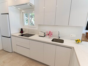 A modern kitchen with white cabinets, a built-in oven, a sink, and a window with a view of greenery. - Beachfront apartment with communal pool and parking in San Pedro de Alcántara (San Pedro Alcántara)