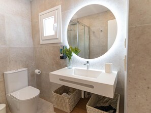 A modern bathroom with a white sink, a round mirror, and a glass-enclosed shower. - Beachfront apartment with communal pool and parking in San Pedro de Alcántara (San Pedro Alcántara)