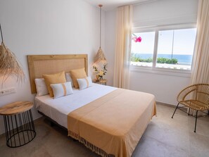 Habitación de hotel con cama, mesita de noche, lámpara, silla y ventana con vistas.