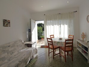 A dining area with a table and chairs, a sofa, and a bookshelf. - Apartment for 4 by the beach with AC and parking (Llançà)