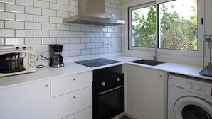 Een kleine keuken met witte kasten, een ingebouwde magnetron, koffiezetapparaat, fornuis, spoelbak en een wasmachine.