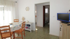 Een kamer met een eettafel, stoelen, een televisie en een deur naar een badkamer.
