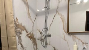 Een badkamer met een marmeren wand, een badkuip, toilet en een wastafel met spiegel erboven.