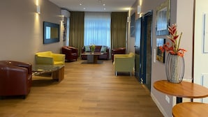 Een moderne hotellobby met een houten vloer, leren banken, een bijzettafeltje en een bloemenvaas.