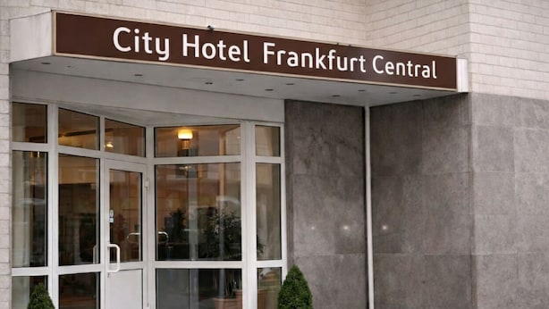 De ingang van Hotel City Frankfurt Centraal, met een glazen deur en plantenbakken.