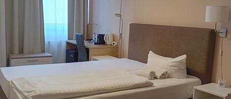 A hotel room with a large bed, a desk, a chair, a lamp, and a bedside table.