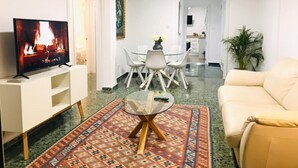 Ett vardagsrum med en tv, en soffa, ett matbord med stolar och ett kök i bakgrunden.