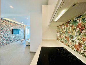 A modern kitchen with a black stovetop, a wall-mounted TV, and a floral wallpaper design. - Bright apartment at Malagueta Beach with terrace (Málaga)