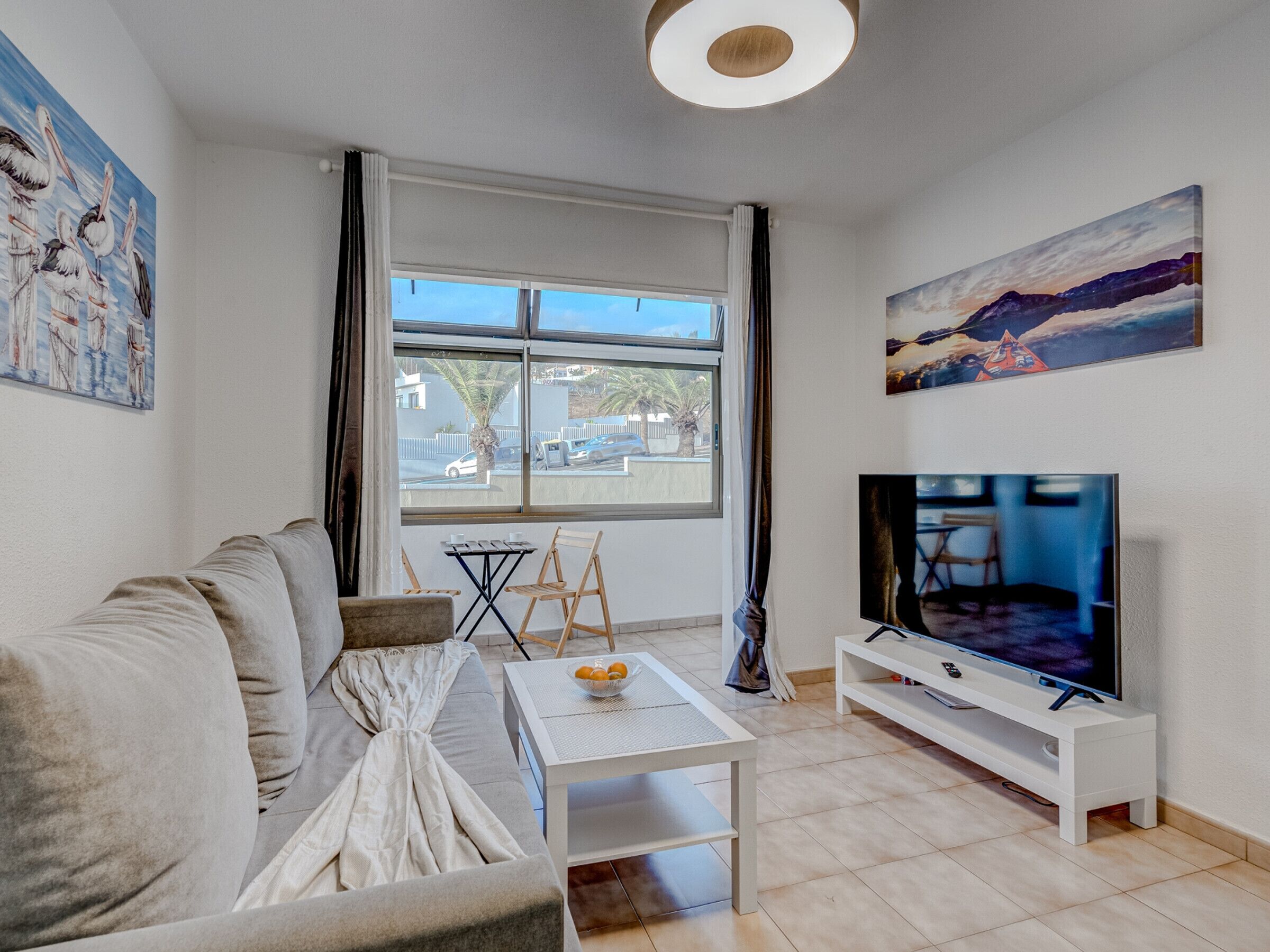 Una sala de estar moderna con un sofá, una mesa de centro, un televisor sobre un mueble blanco y obras de arte en las paredes.