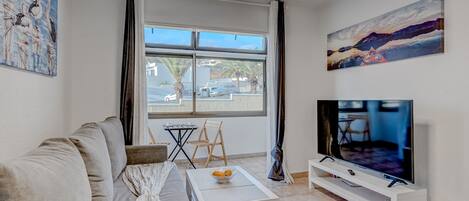 Una sala de estar moderna con un sofá, una mesa de centro, un televisor sobre un mueble blanco y obras de arte en las paredes.