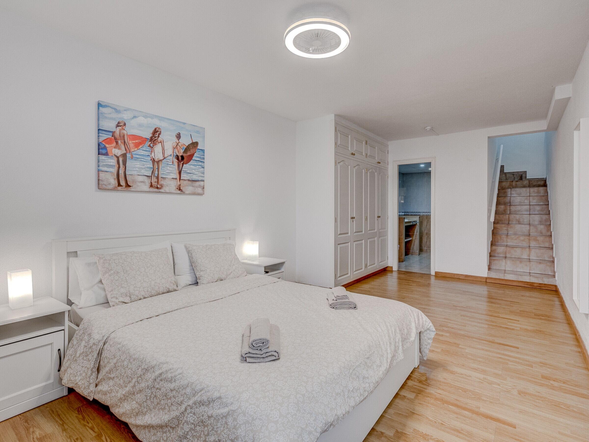 A bedroom with a bed, a nightstand, a painting, a wardrobe, and a staircase.