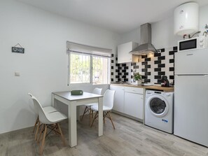 A modern kitchen with a built-in washing machine, a dining area with a table and chairs, and a window with blinds. - Modern and functional apartment in Malaga, near beaches (Málaga)