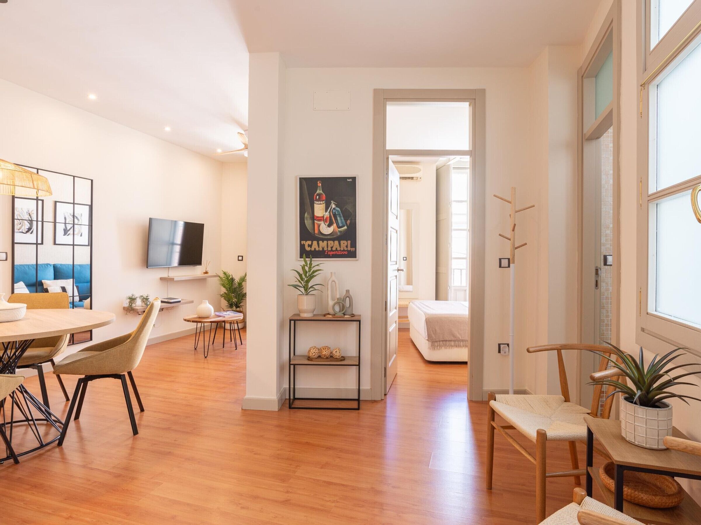 Un espacio de sala moderno con comedor, un televisor montado en la pared y un pasillo que conduce a otra habitación.